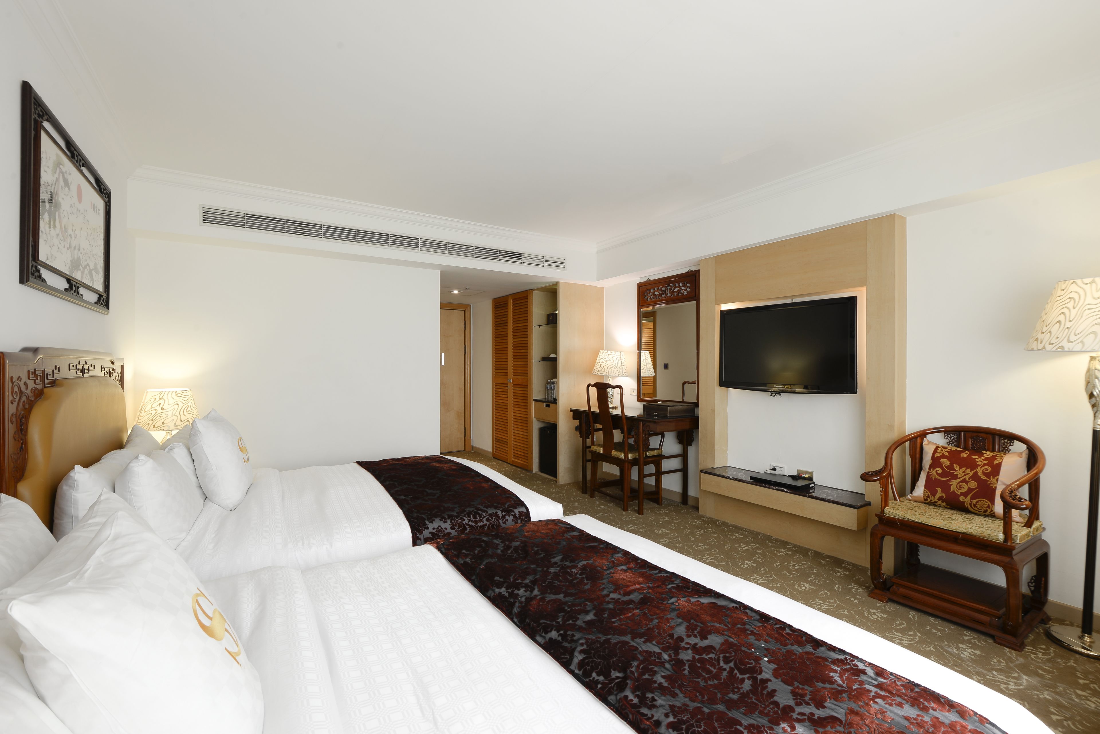 A hotel room with two beds, a desk with a chair, a TV, and a lamp.
