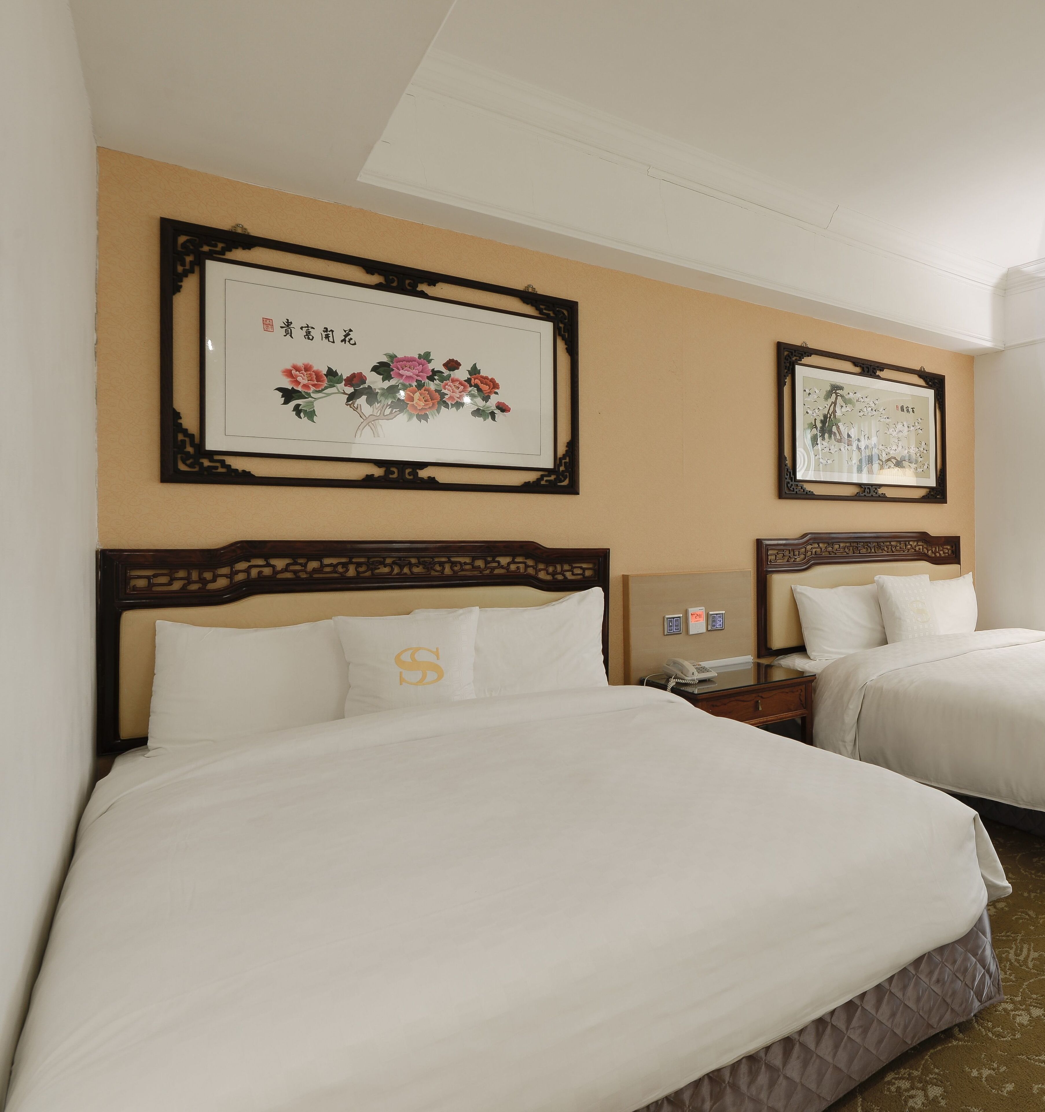 Une chambre d’hôtel avec deux lits, chacun doté d’une tête de lit en bois et de linge de lit blanc. Des œuvres d’art encadrées ornent les murs au-dessus des lits.