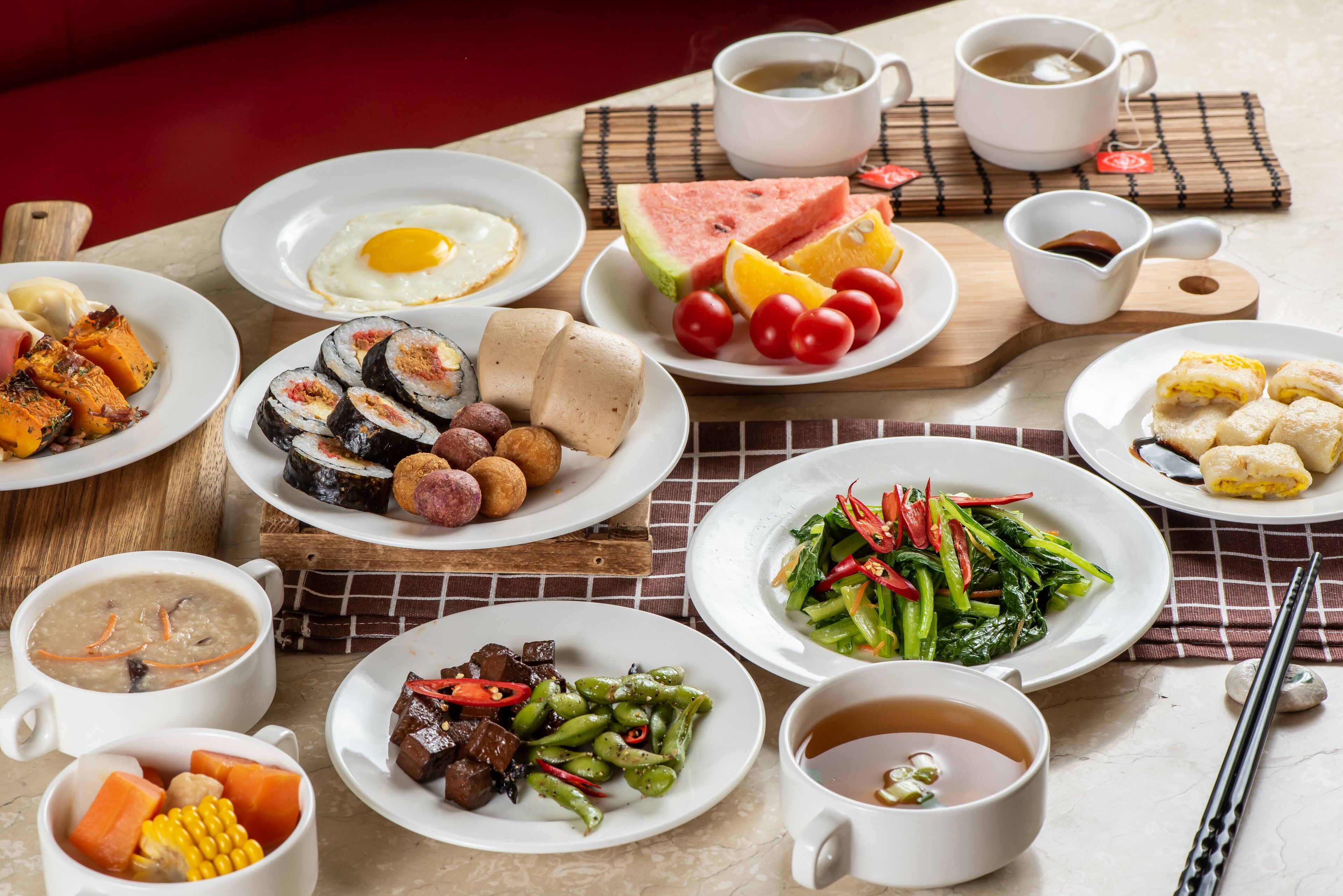 Une table garnie de divers plats, notamment des sushis, des œufs et des légumes, ainsi que des tasses de thé et de café.
