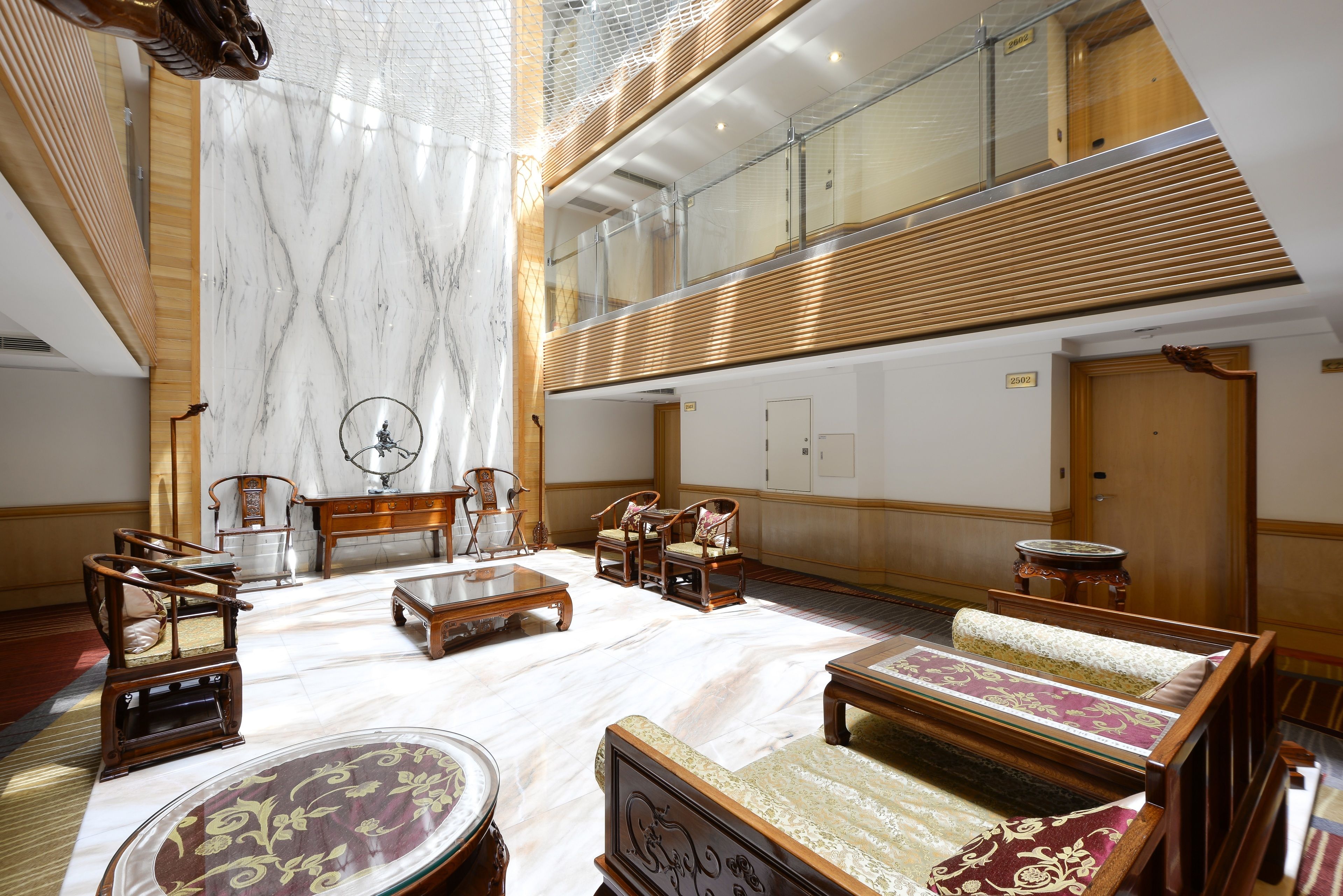 A spacious lobby with a high ceiling, marble flooring, and a seating area with wooden furniture.
