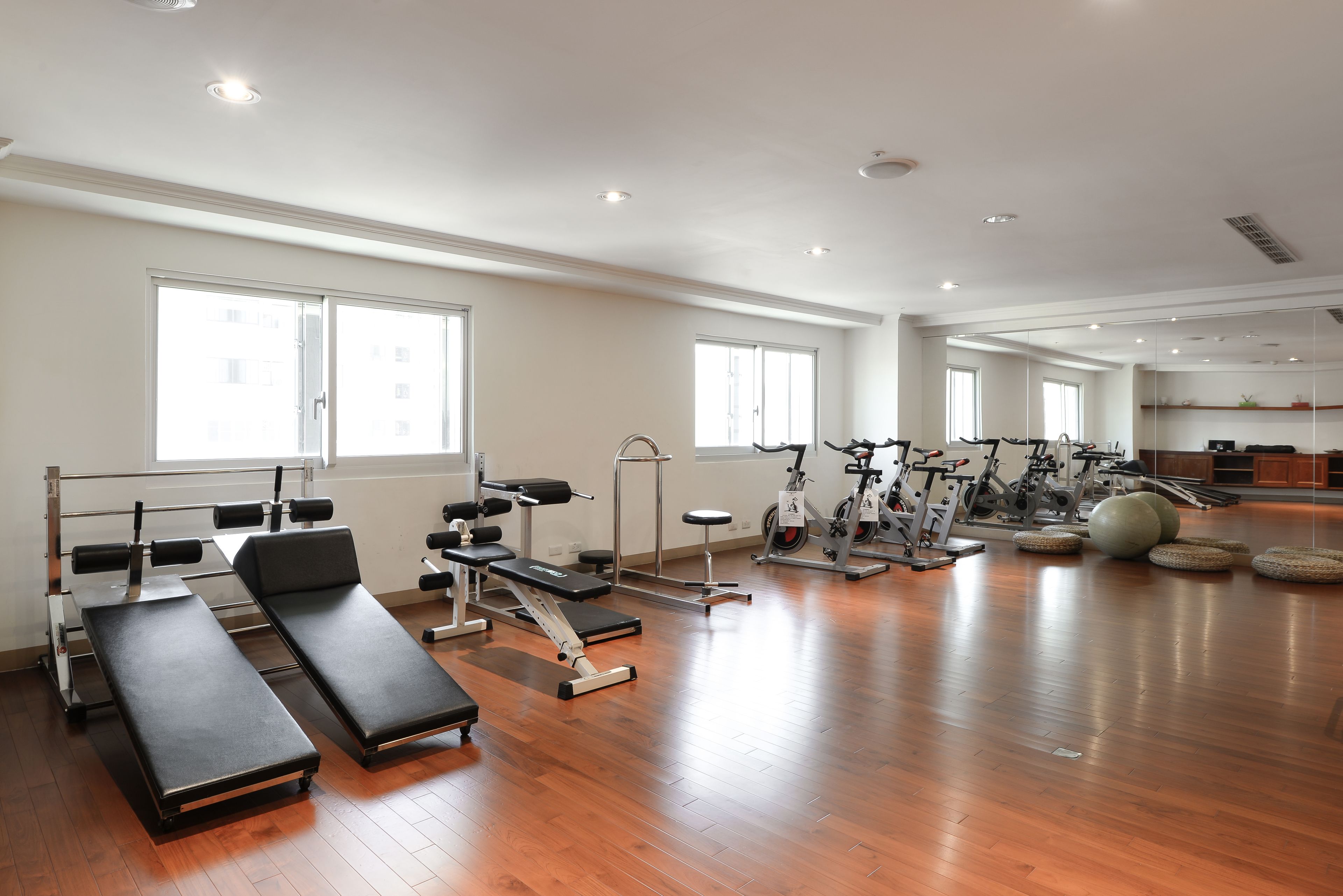 Un gimnasio amplio con equipo de ejercicio, ventanas grandes y pisos de madera.
