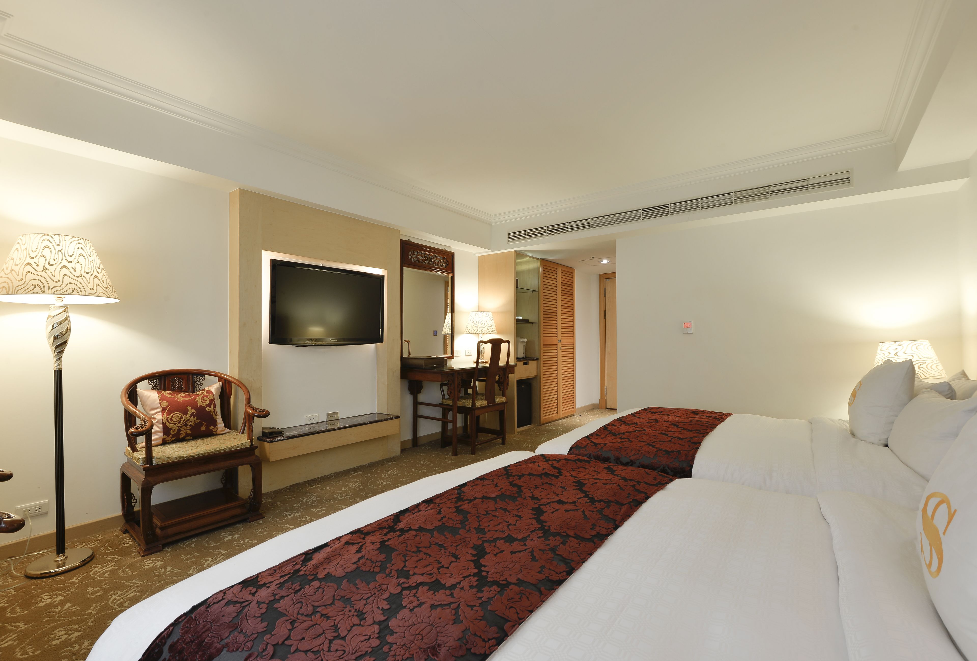 A hotel room with two beds, a desk, a chair, a TV, and a mirror.