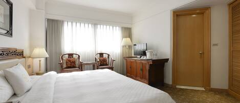Habitación de hotel con una cama grande, dos sillas, un escritorio con lámpara, televisión y armario.