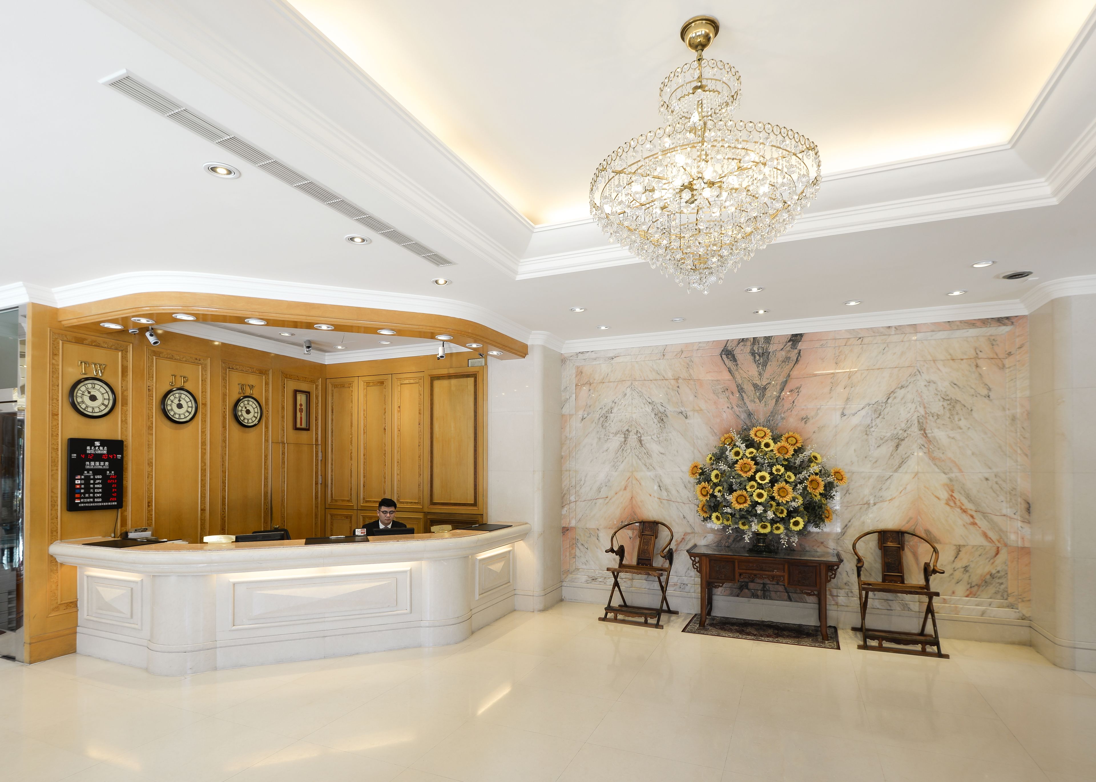 A hotel lobby with a reception desk, a chandelier, a clock, and a marble wall.