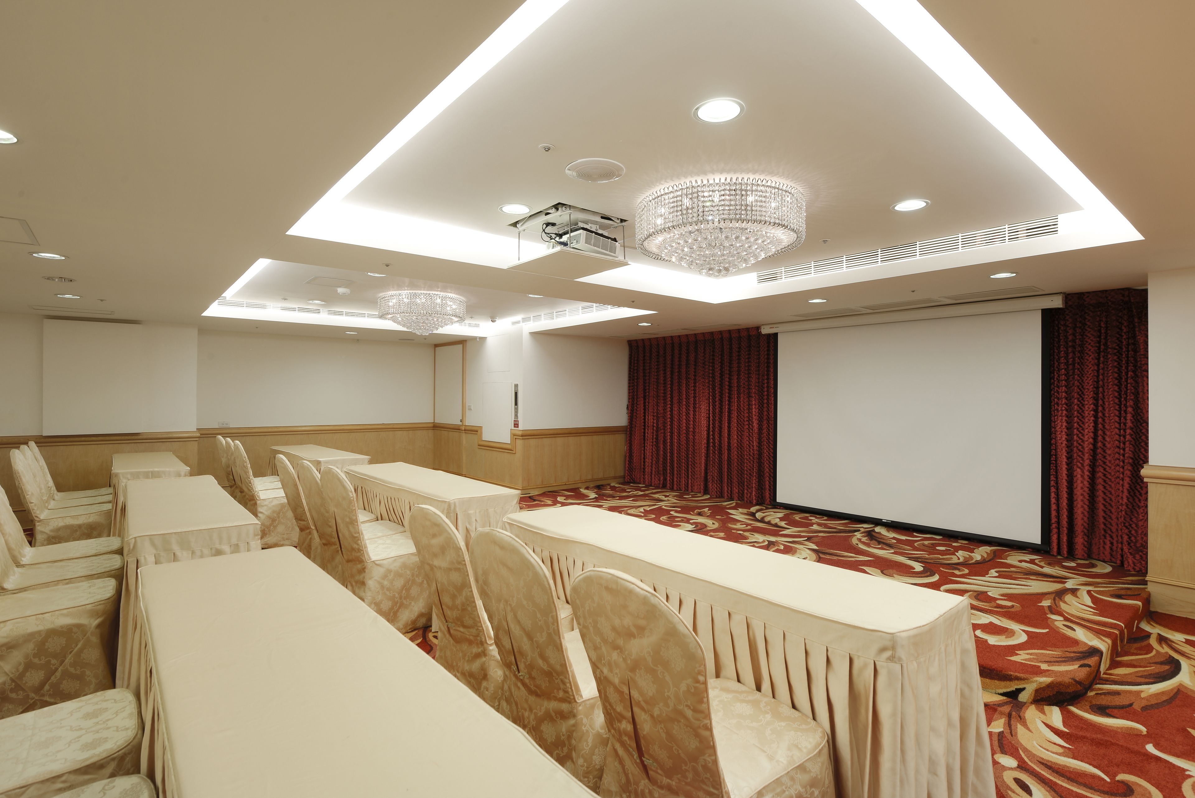 A conference room with tables and chairs, a large screen, and a carpeted floor.
