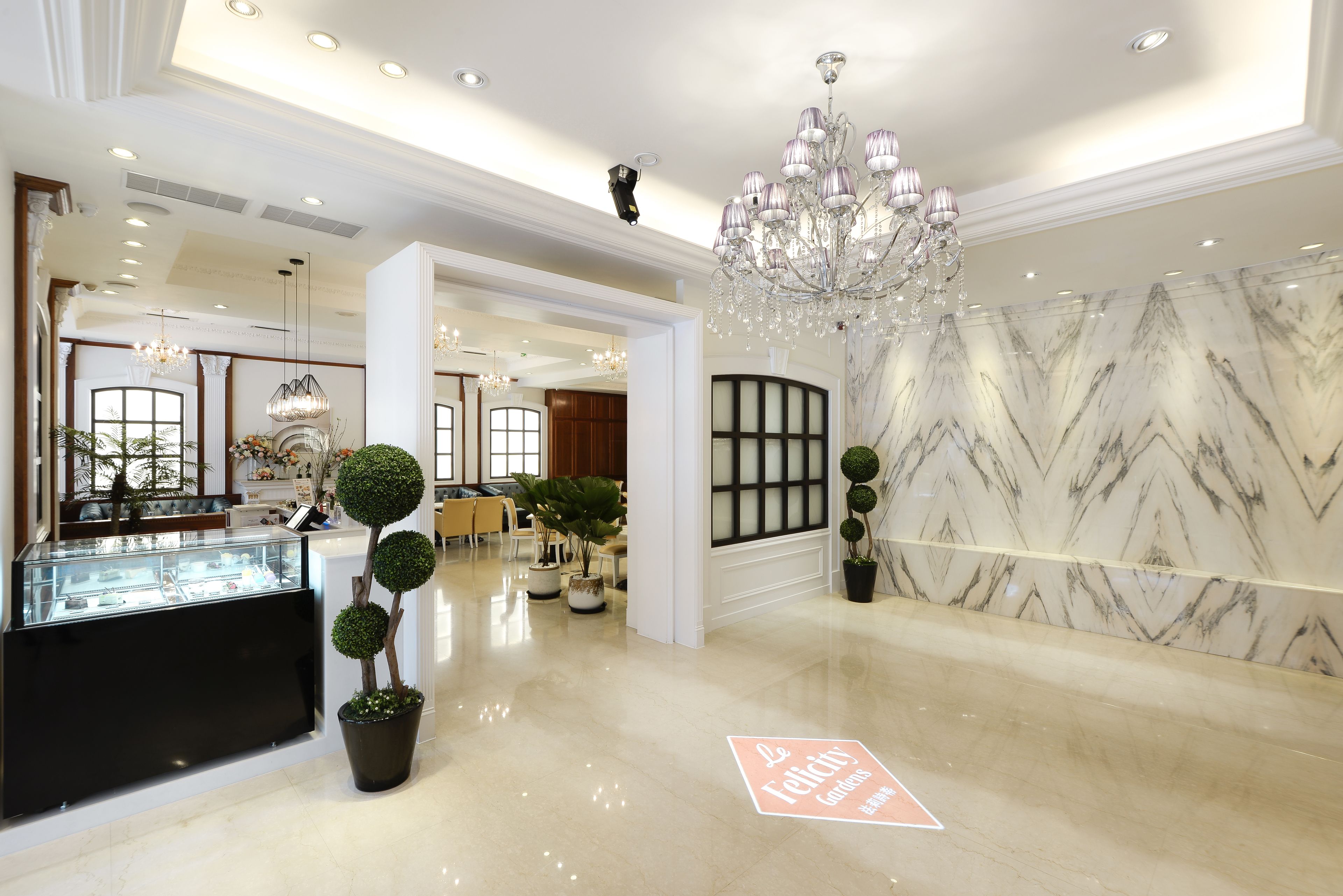 A spacious lobby with a marble wall, a reception desk, and a chandelier.