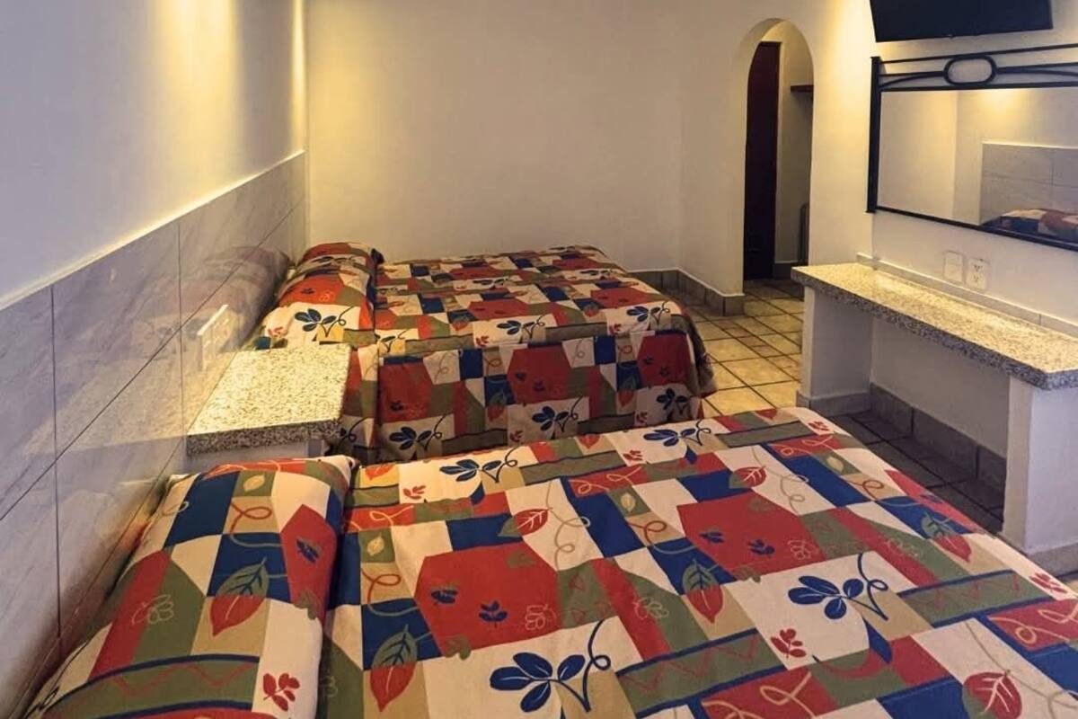 Une chambre d’hôtel avec un lit, un petit bureau, une télévision et un sol carrelé.