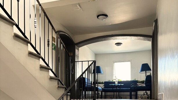 Eine Treppe mit schwarzen Geländern führt zu einem Wohnbereich mit einem blauen Sofa und einer Lampe.