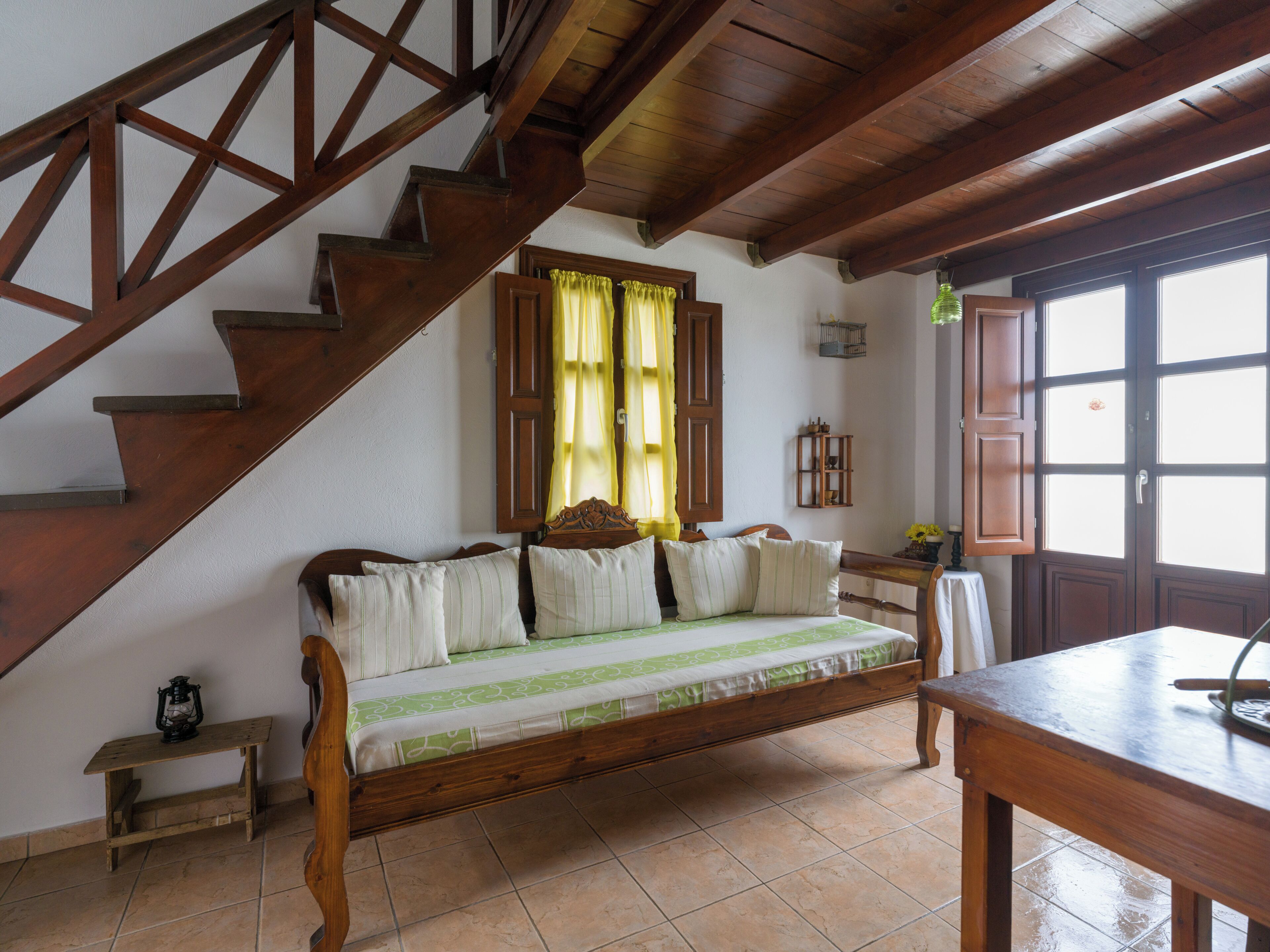 Un escalier en bois mène à une pièce où se trouvent un lit, une petite table et une fenêtre avec des rideaux.
