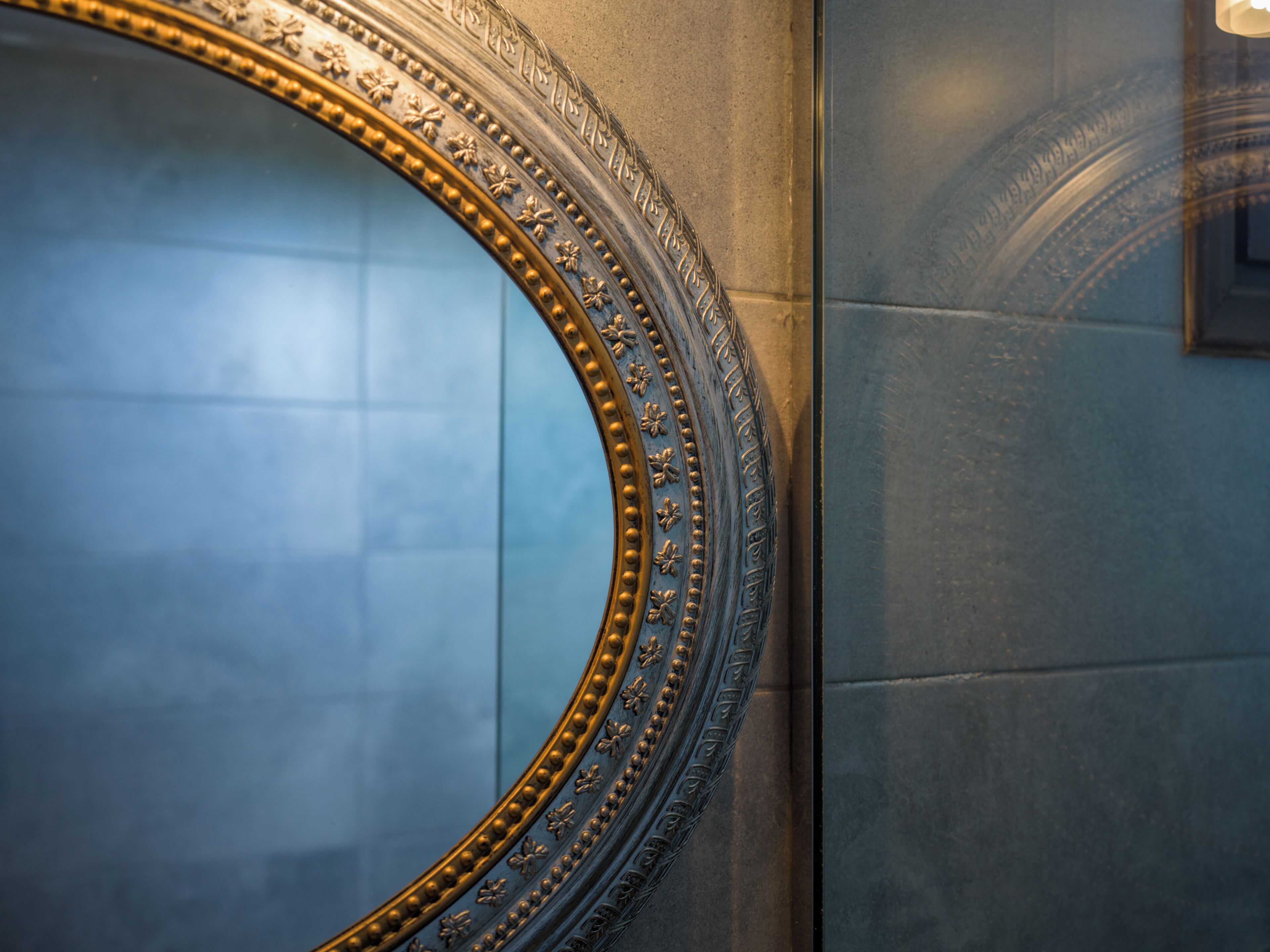 A large, ornate mirror with a gold frame and intricate designs, mounted on a textured wall.