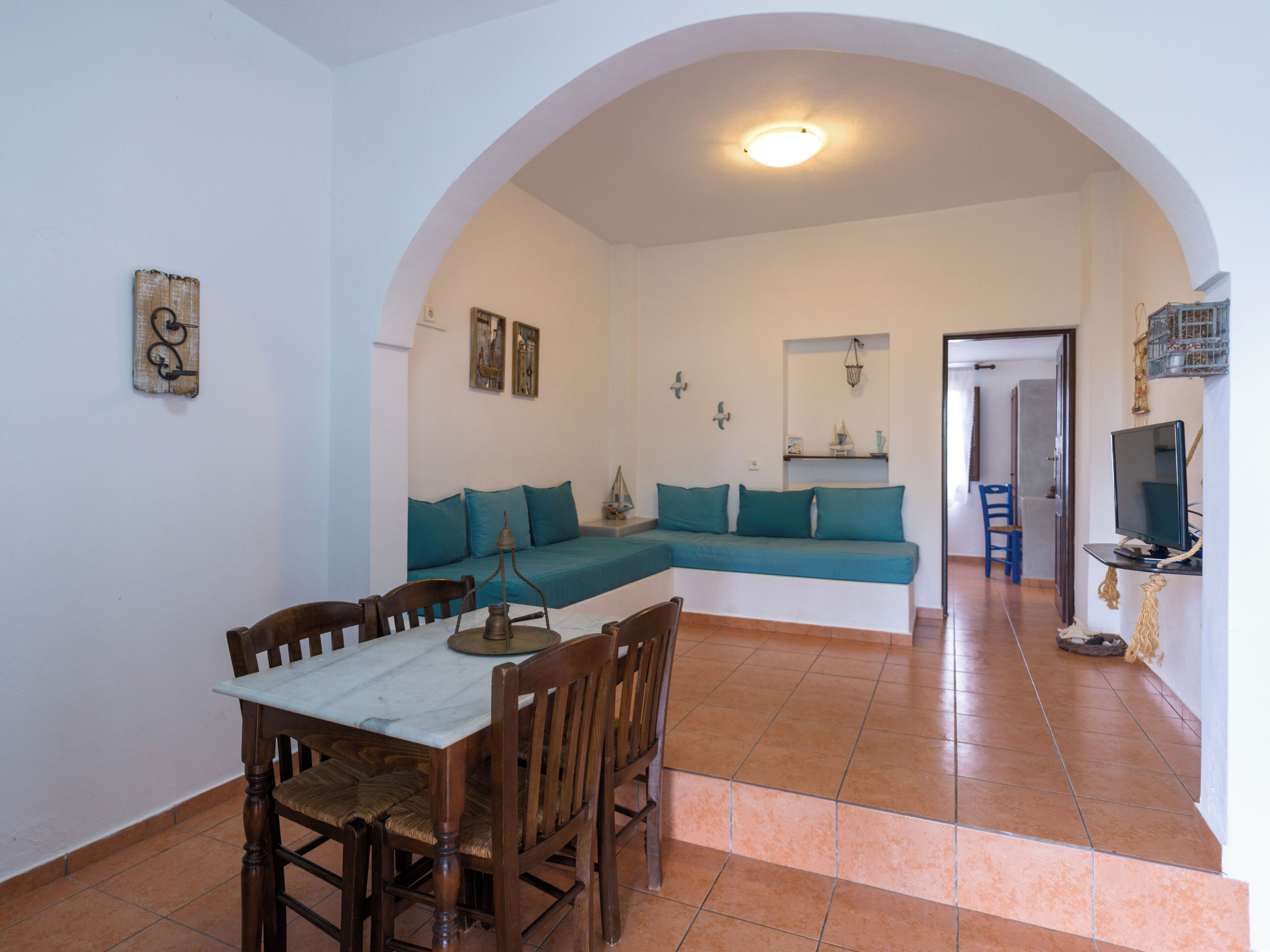 A dining area with a table and chairs, a sofa with teal cushions, and a television on a stand.