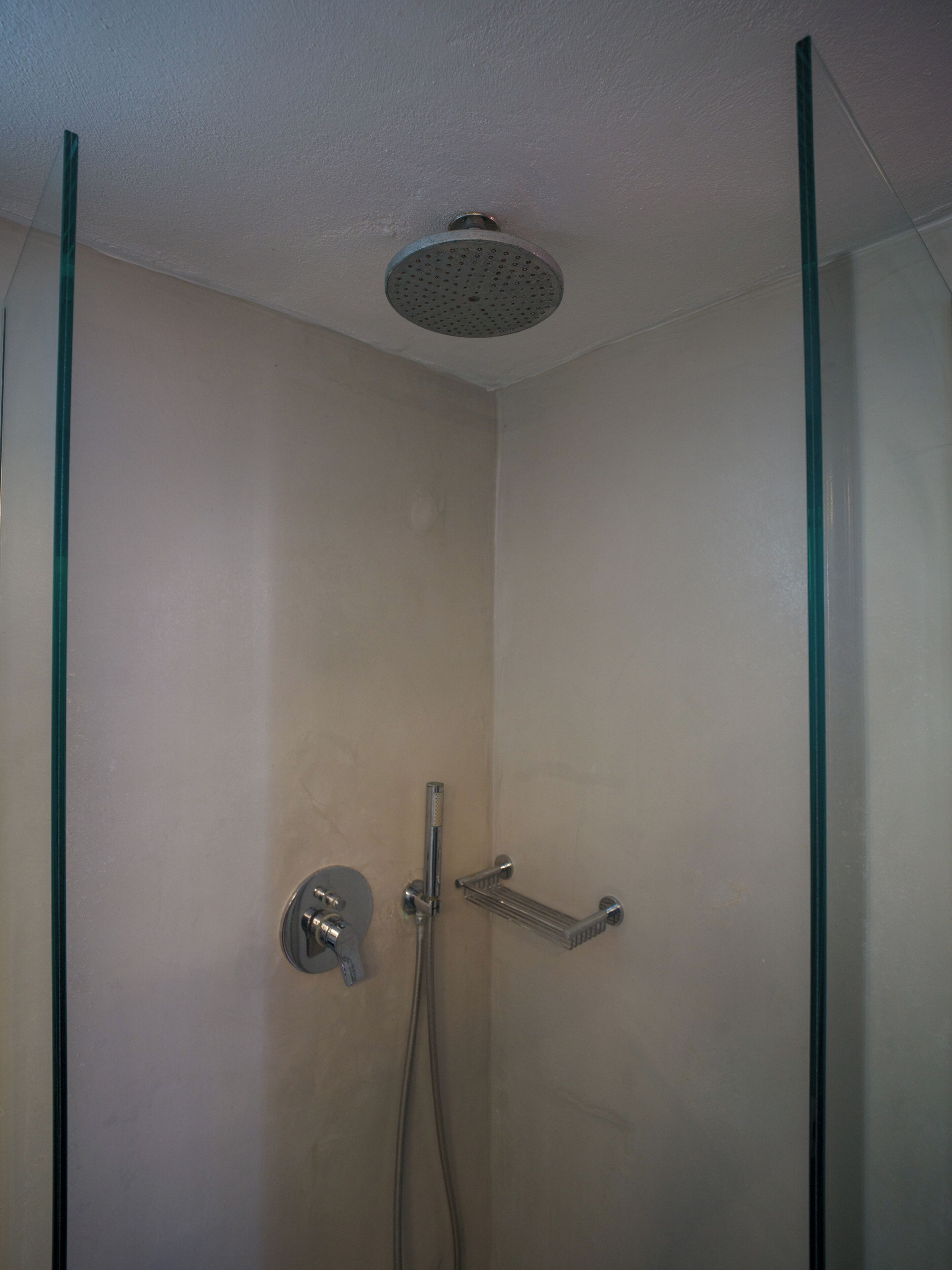 Una ducha con cabezal de ducha manual, grifería empotrada en la pared y zona de ducha con mampara de vidrio.