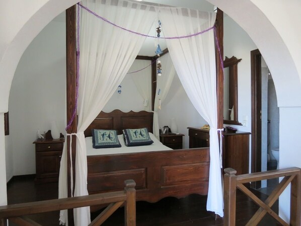 A four-poster bed with a canopy, wooden headboard, bedside tables, and a mirror.