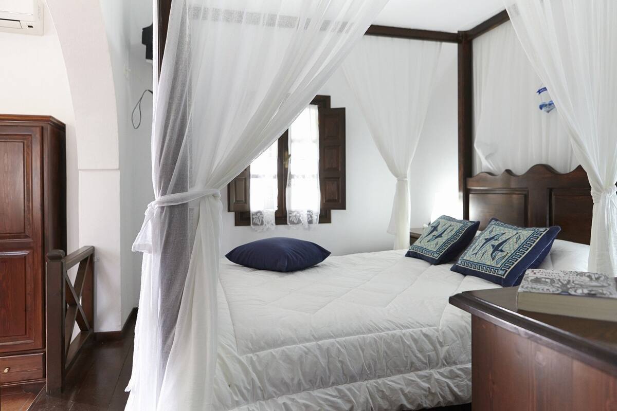 A bedroom with a bed, a wooden headboard, a nightstand, and a window with a view.