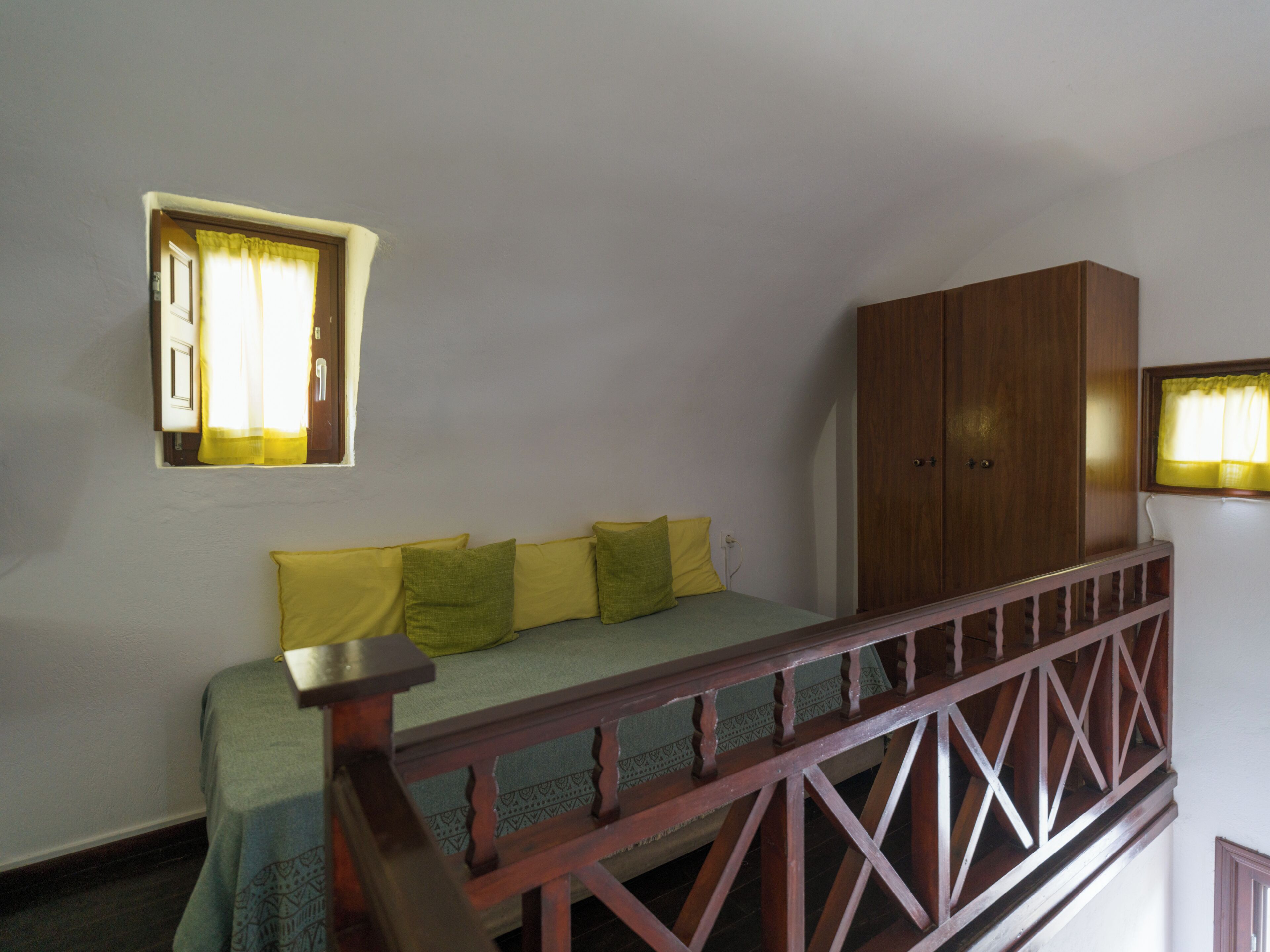 A room with a bed, a wooden wardrobe, and a window with curtains.