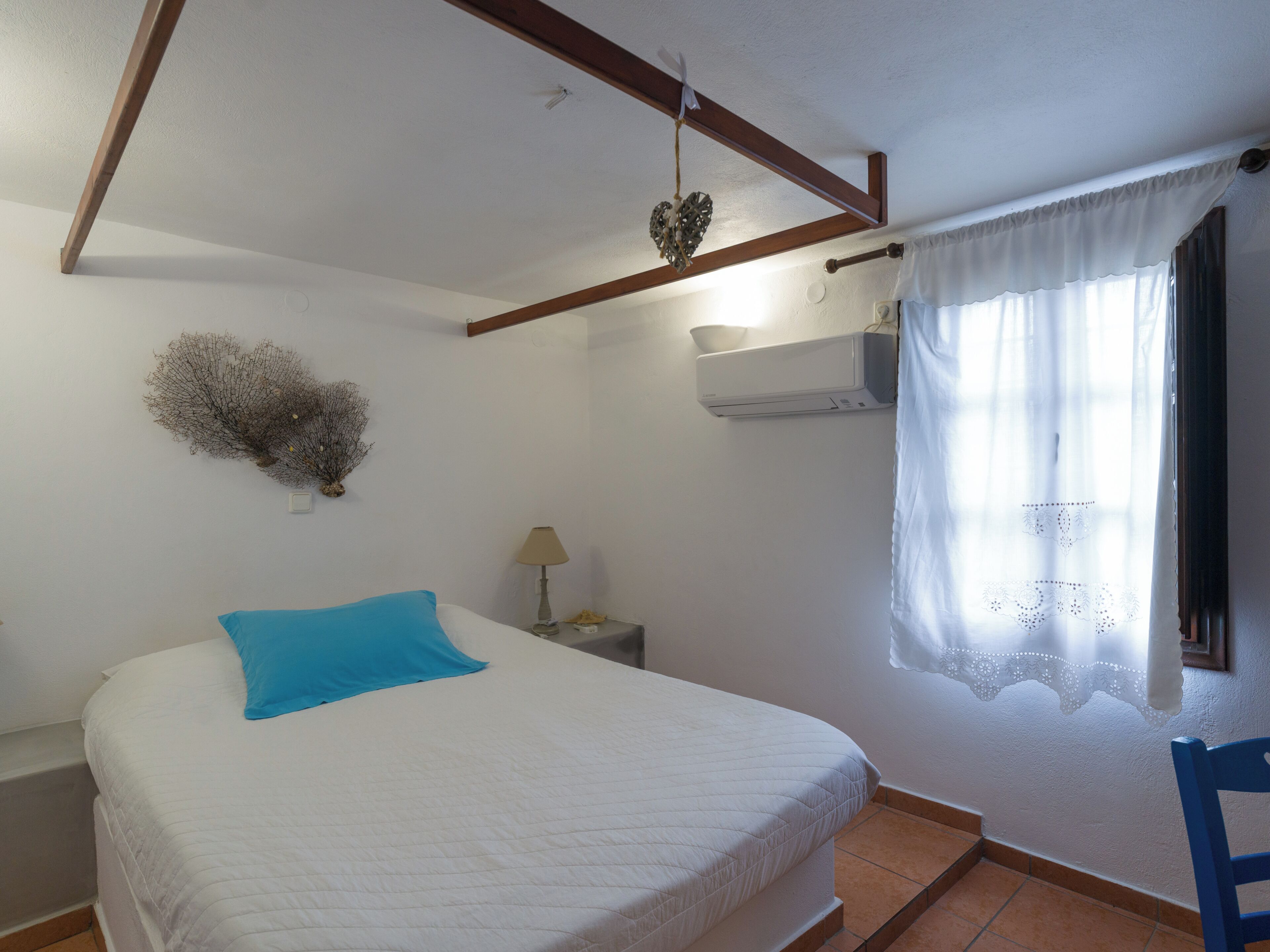 Une chambre à coucher comprenant un lit, une table de chevet, une lampe, un climatiseur fixé au mur et une fenêtre avec un rideau.
