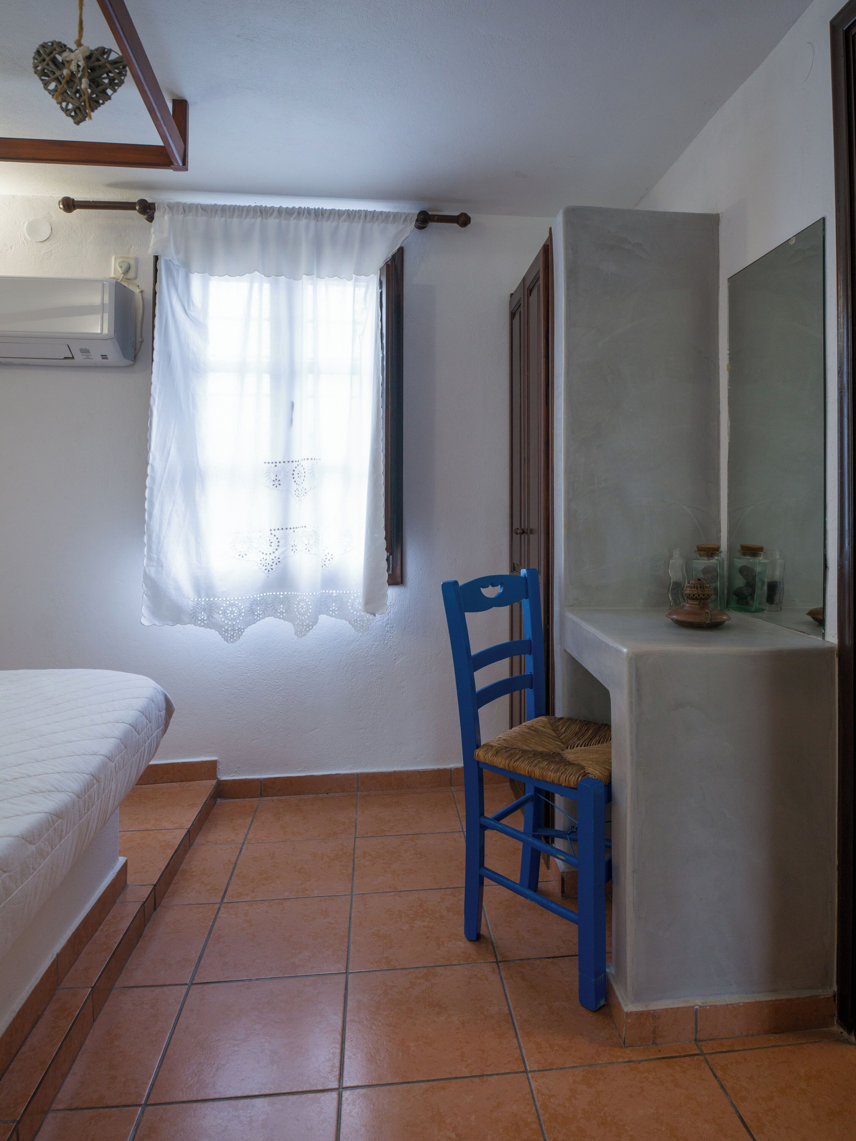Un dormitorio con una cama, una silla, una ventana con cortina y un espejo en la pared.
