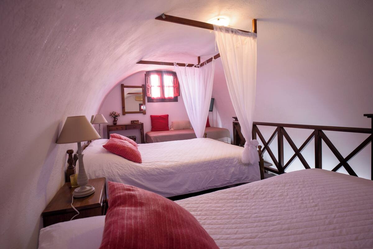 A bedroom with two beds, a nightstand, a lamp, a mirror, and a window with curtains.