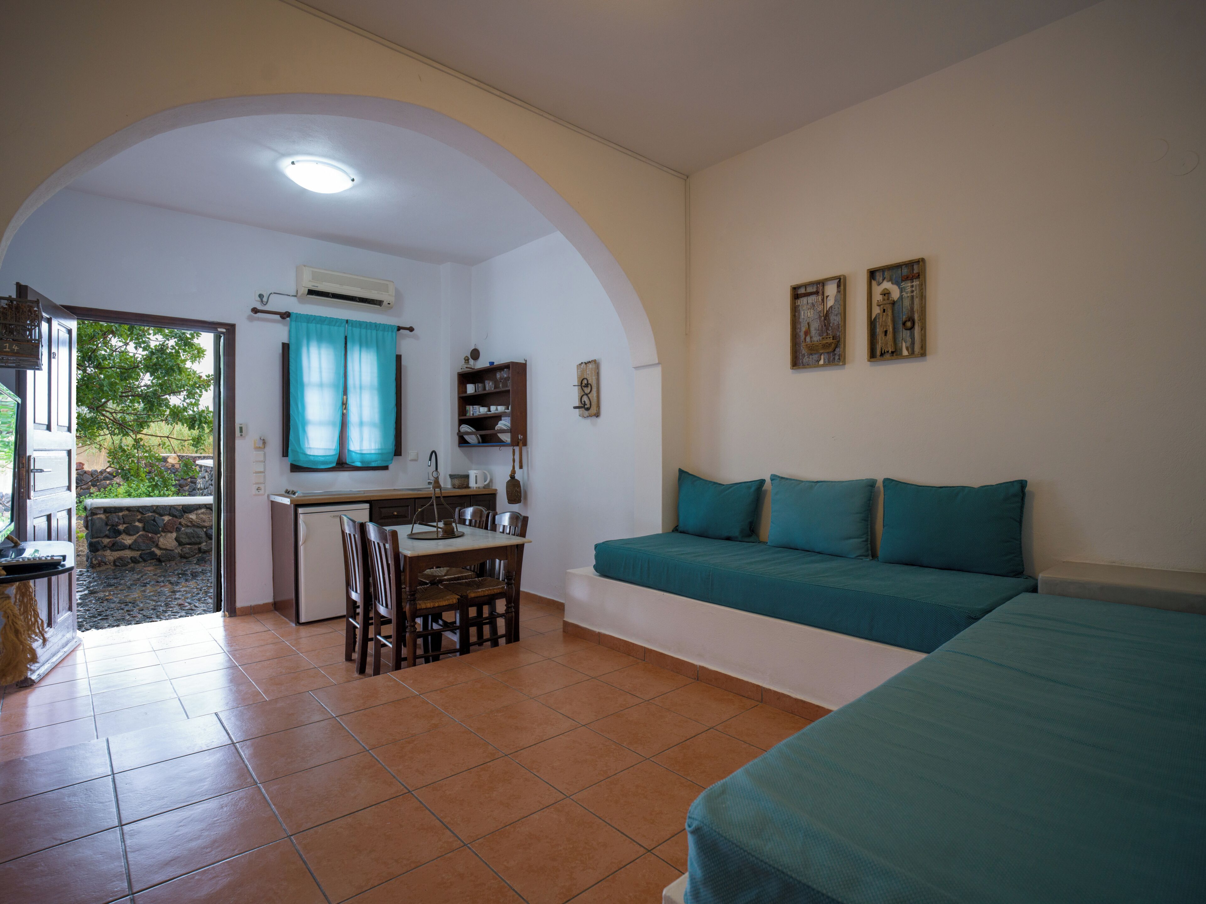 A room with a dining table, chairs, a sofa, a kitchen area, and a view through an open door.