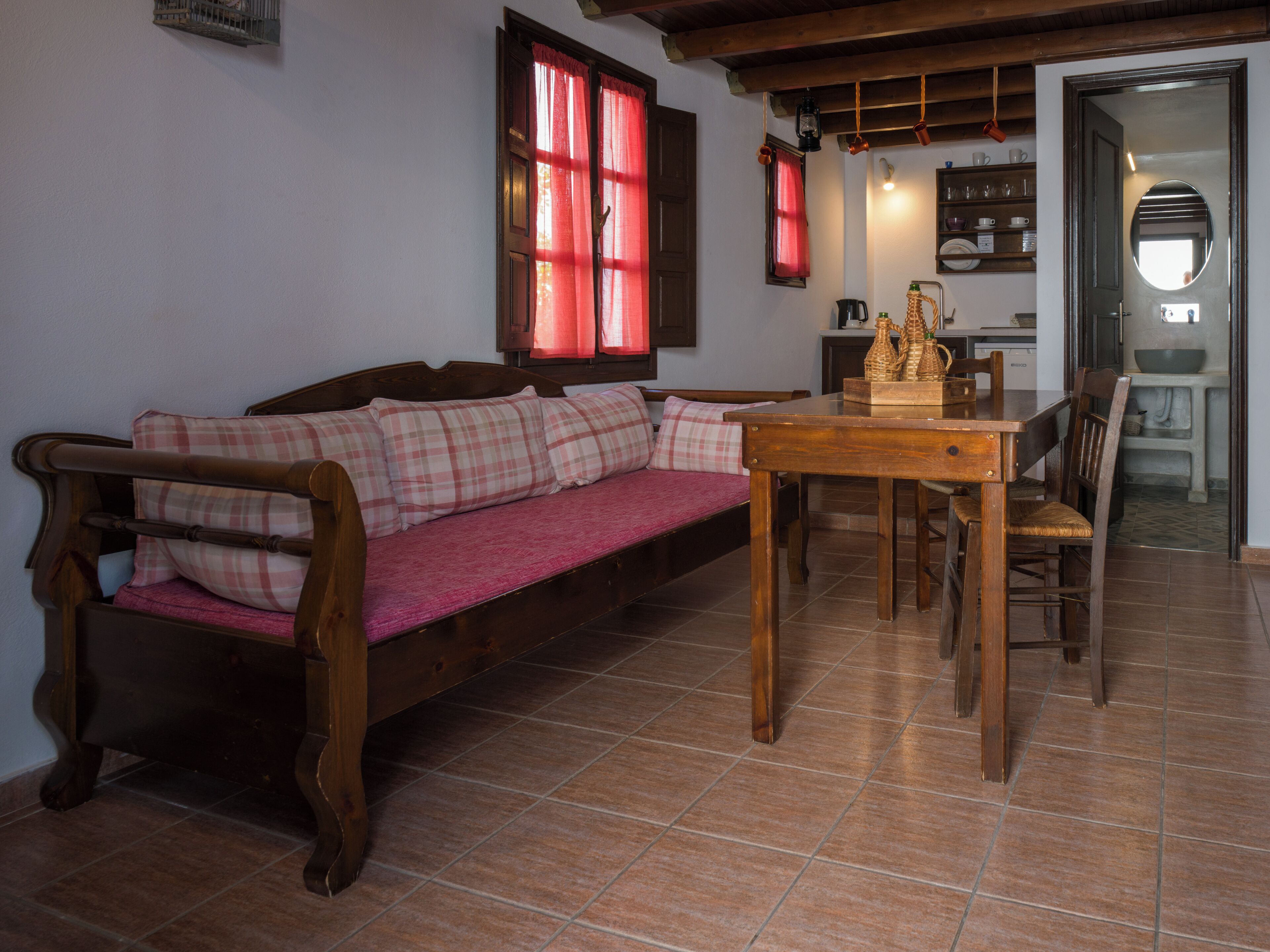 Une pièce chaleureuse avec un banc en bois, une table à manger et un coin cuisine visible à travers une porte ouverte.