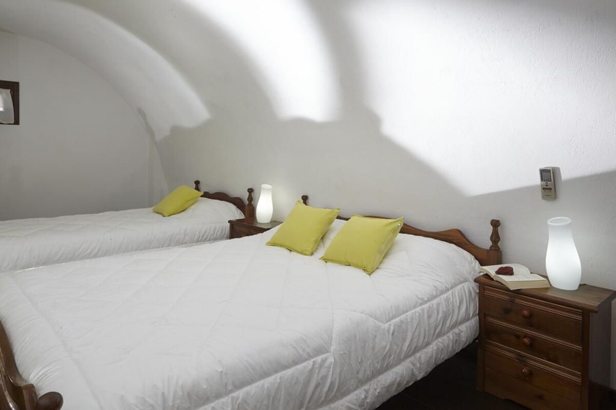 A hotel room with two beds, a nightstand, a bedside lamp, and a wall-mounted thermostat.