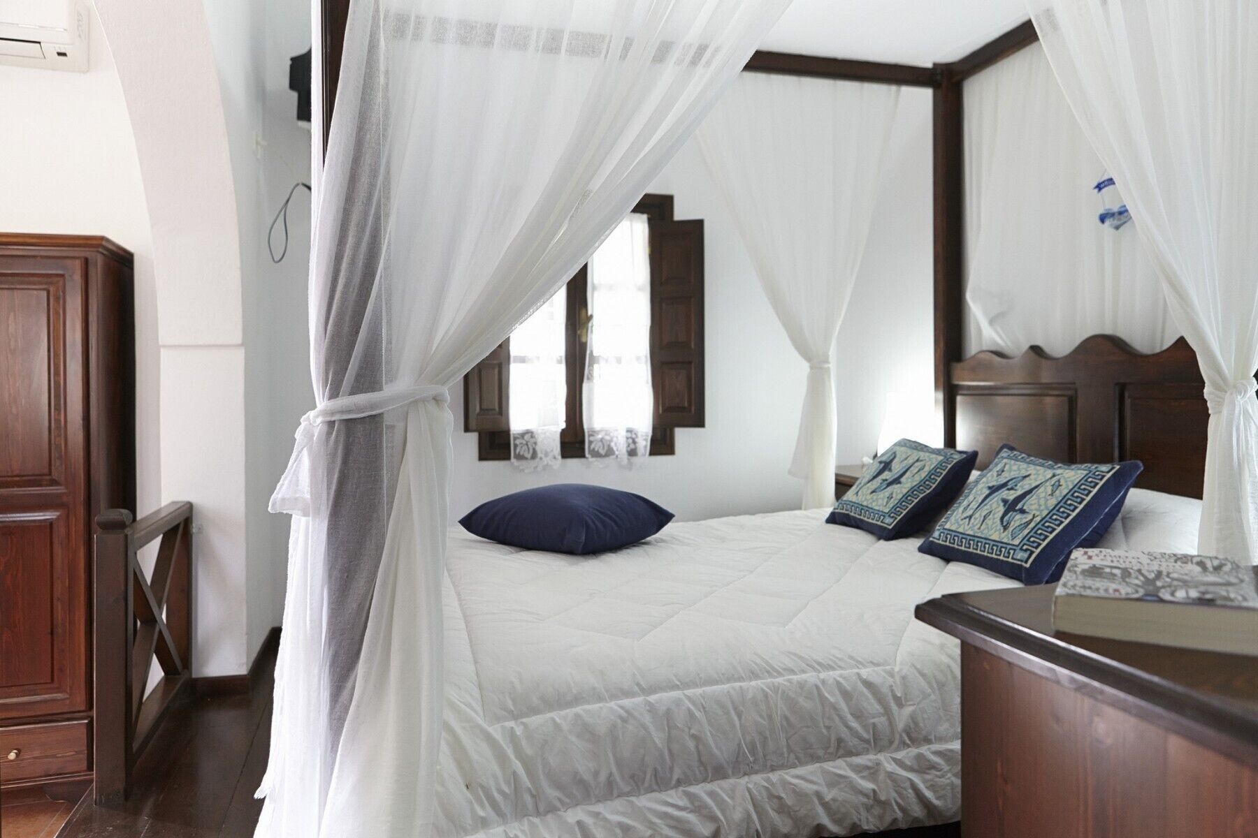 A bedroom with a bed, a wooden headboard, a nightstand, and a window with curtains.