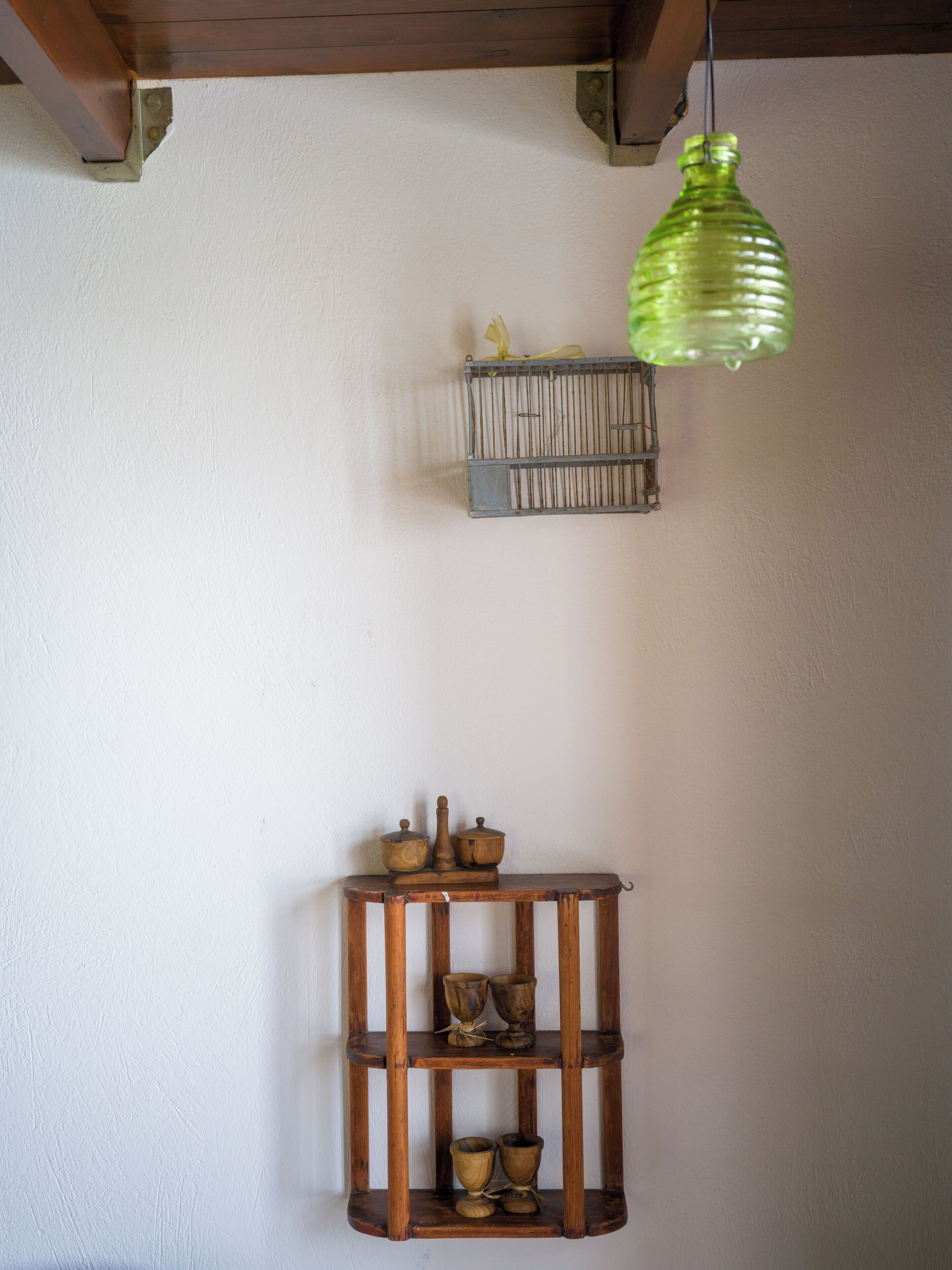 A wooden shelf with pottery and a hanging green glass bottle.