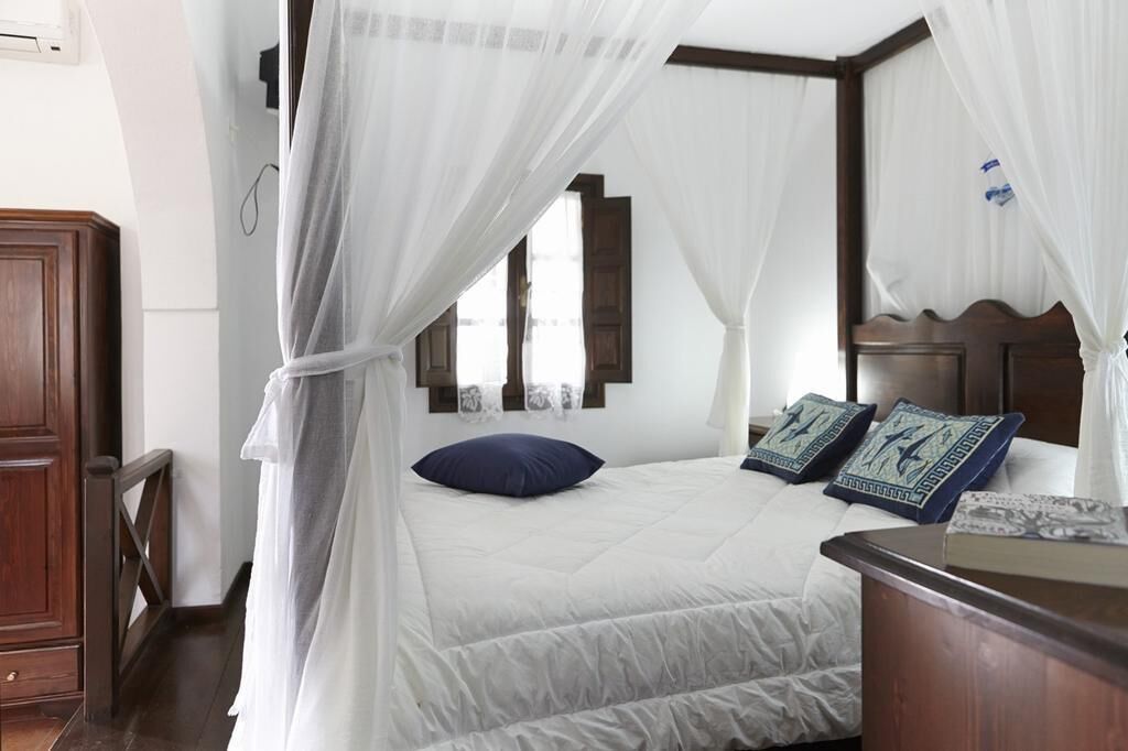 A bedroom with a bed, a nightstand, a wooden headboard, and a window with curtains.