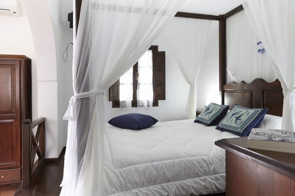 A bedroom with a bed, a nightstand, a wooden headboard, and a window with curtains.