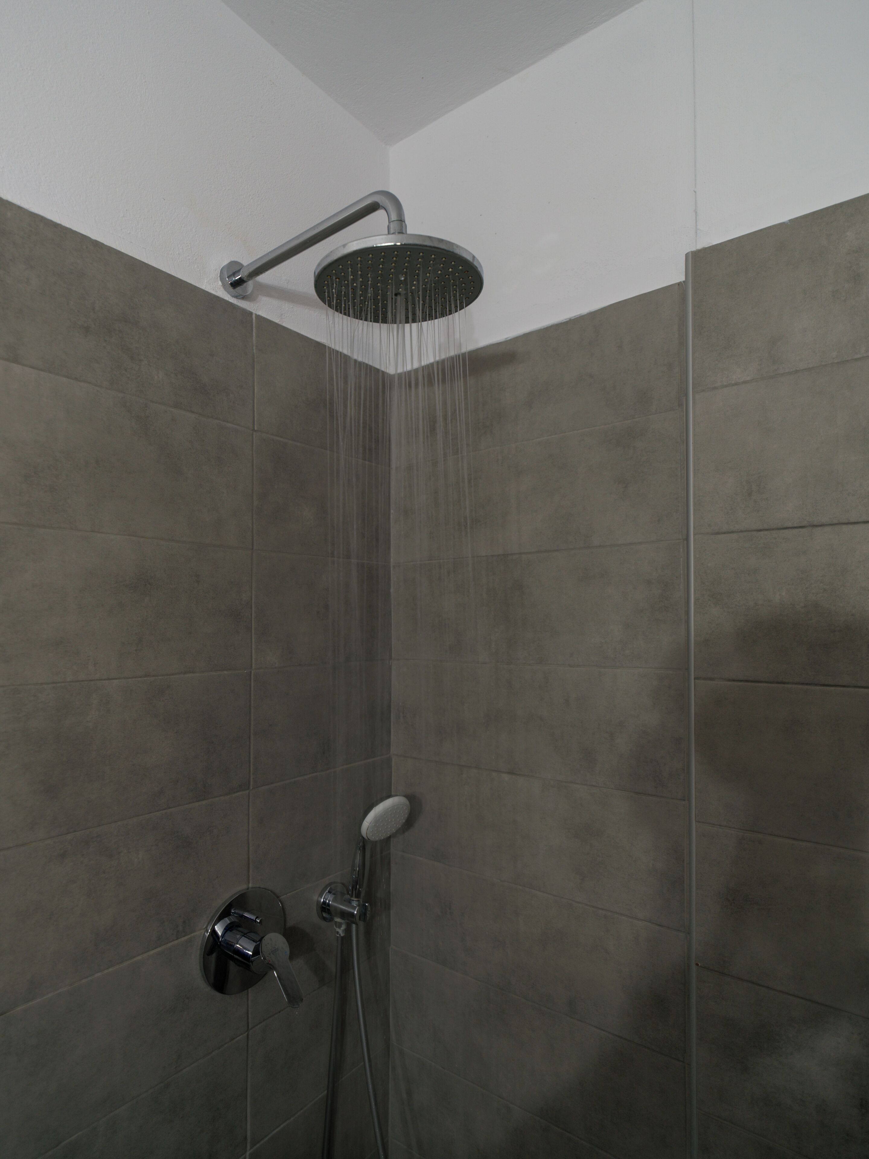 A shower with a rain head, a handheld showerhead, and a wall-mounted control valve.