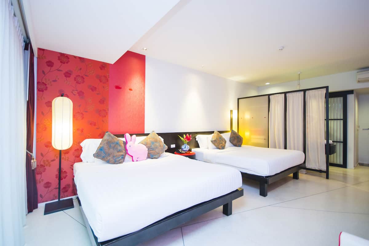 A hotel room with two beds, a red floral wall, a modern lamp, and a view of the outside.
