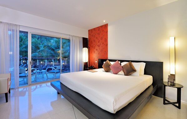 A modern hotel room with a large bed, a nightstand, a lamp, and a view of a pool and palm trees through the glass door.