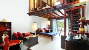 A spacious living area with a sofa, a coffee table, and a dining table. There is a staircase leading to an upper level. - Red Ginger Chic Resort (Krabi)