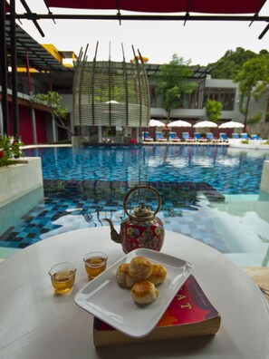 Una mesa con tetera, galletas y una taza de té, con vistas a una piscina con sillones de baño y sombrillas.