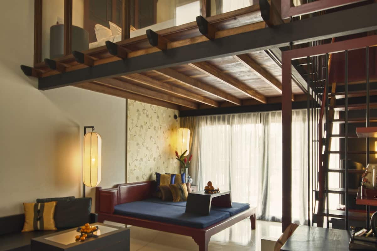 A spacious living area with a high ceiling, a sofa set, a coffee table, and a staircase leading to an upper level.