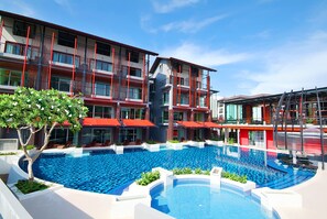 Un hotel moderno con una amplia piscina exterior, varios balcones y toldos rojos.
