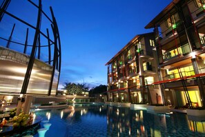 Un hotel moderno con piscina, varios balcones y un exterior bien iluminado al anochecer.