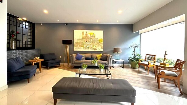 A modern living room with a sofa, armchair, coffee table, and a painting on the wall. - Hotel Arboledas Expo (Guadalajara)