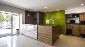 A hotel reception area with a modern design, including a reception desk, a green accent wall, and a clock on the wall. - Hotel Arboledas Expo (Guadalajara)