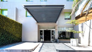 A modern building with a covered entrance, a green hedge, and a potted plant. - Hotel Arboledas Expo (Guadalajara)