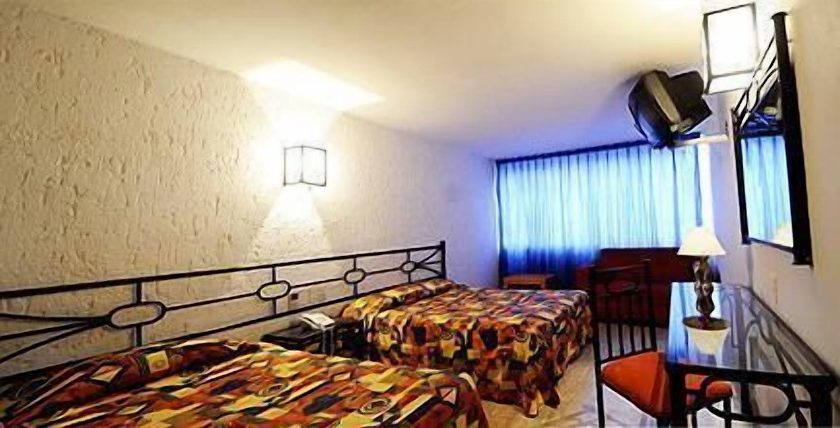 Een hotelkamer met twee bedden, een bureau, een stoel, een lamp, een televisie en een raam met gordijnen.