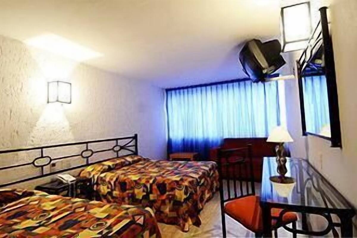 A hotel room with two beds, a desk, a chair, a lamp, a TV, and a window with curtains.