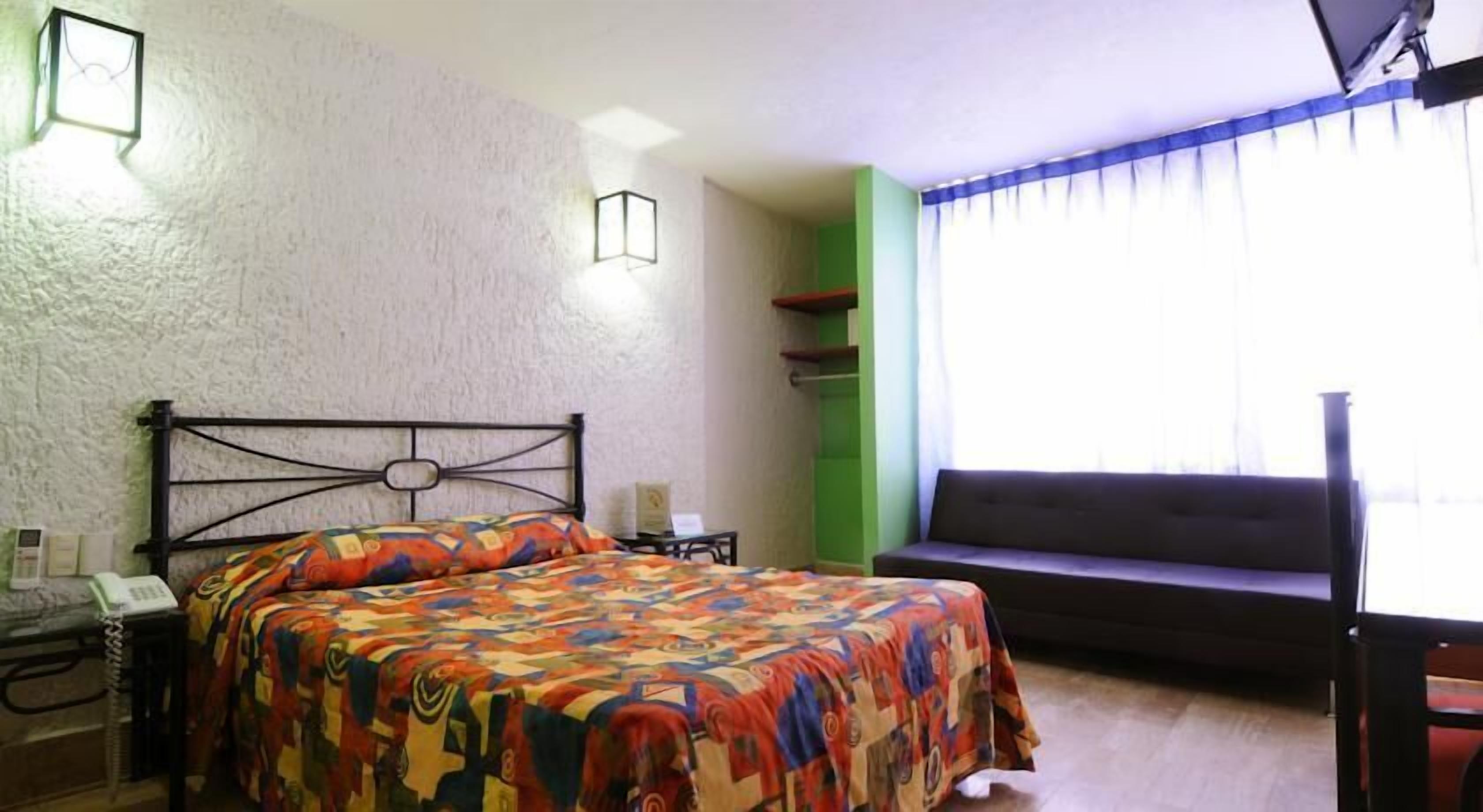 Een slaapkamer met een bed, nachtkastje, lamp, bank en een raam met gordijnen.