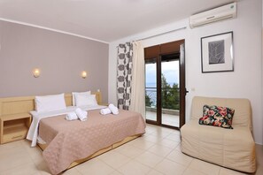A hotel room with a bed, a sofa, a balcony with a view, and an air conditioning unit. - Peristeridis Apartments (Kassandra)