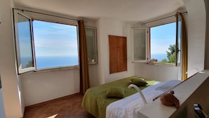 Un dormitorio con cama, mesita de noche, espejo y ventana con cortinas.