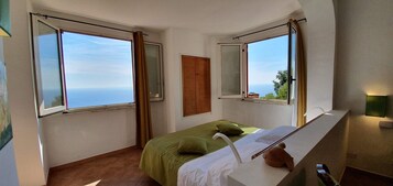 Un dormitorio con cama, mesita de noche, espejo y ventana con cortinas.