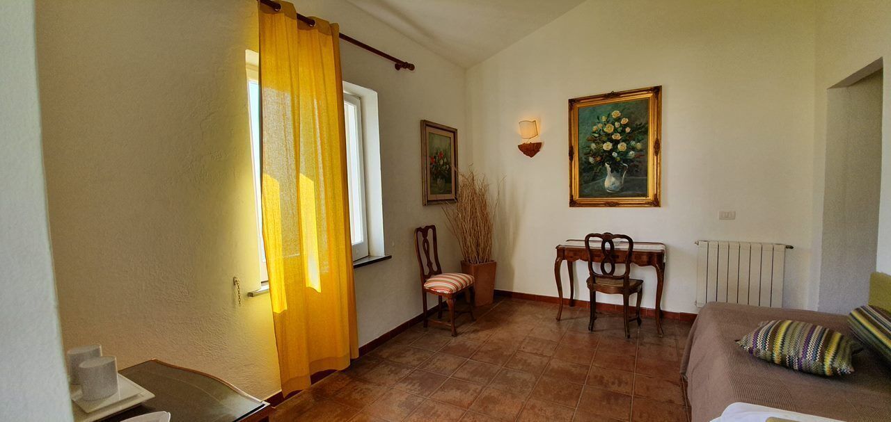 A room with a bed, a chair, a table, a radiator, and a window with curtains.