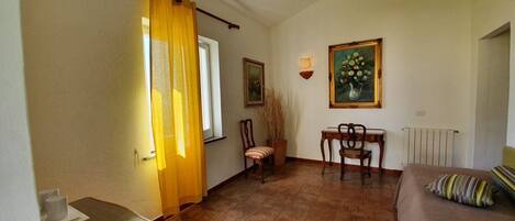 A room with a bed, a chair, a table, a radiator, and a window with curtains.