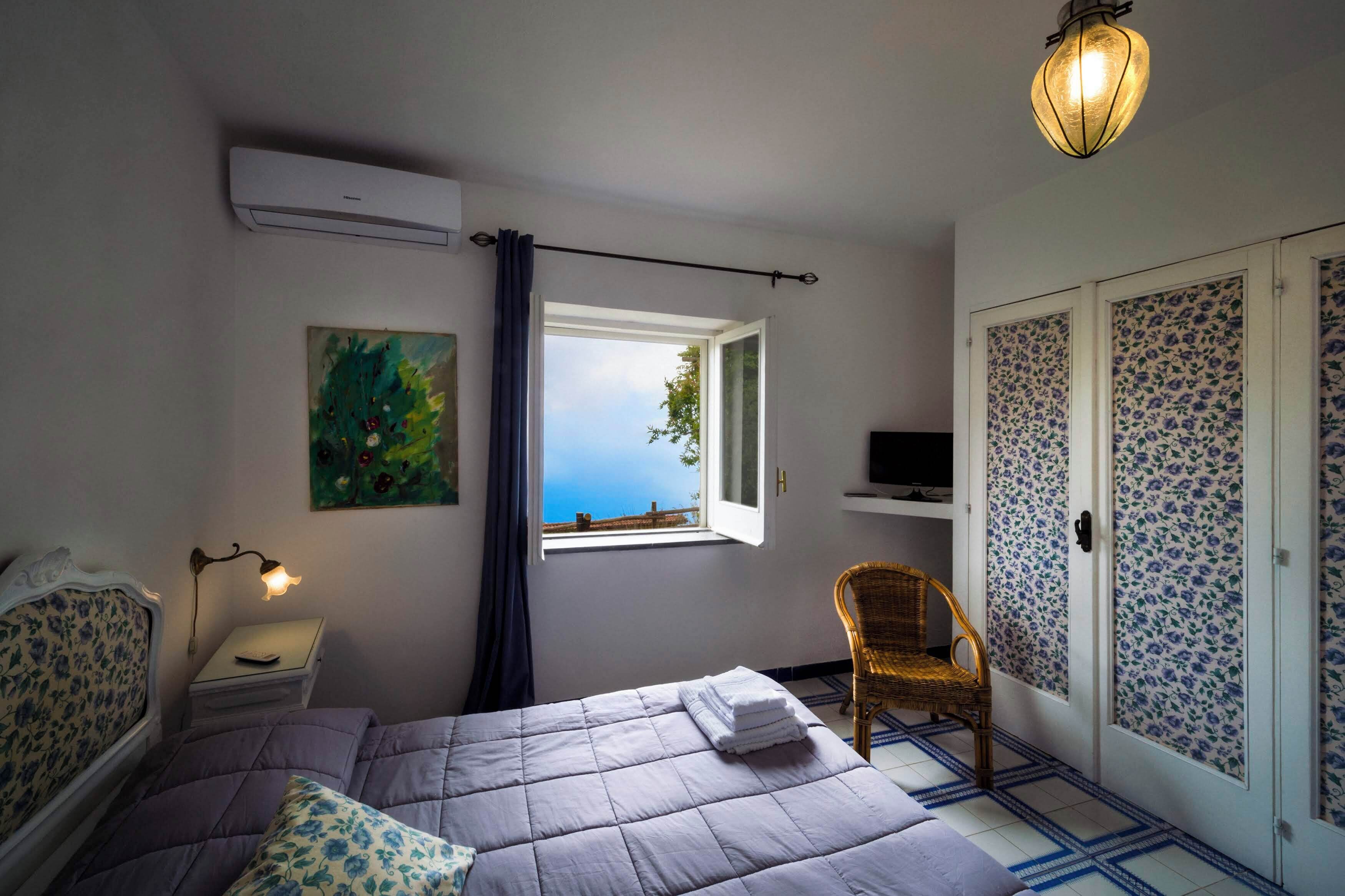 A bedroom with a bed, a nightstand, a lamp, a chair, a TV, a window with a view, and a wardrobe with patterned doors.