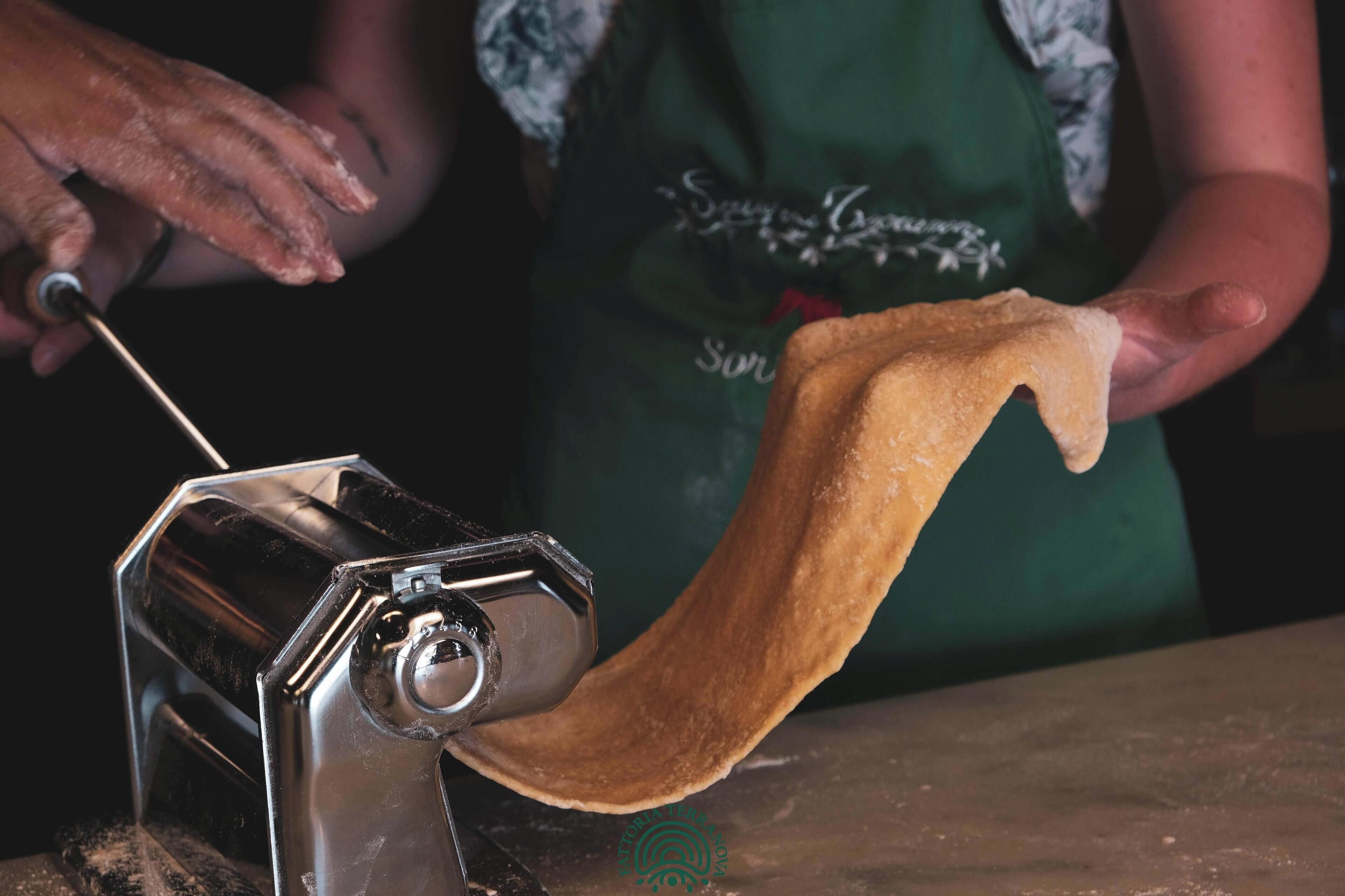 Una persona usando una máquina de pasta para estirar la masa.